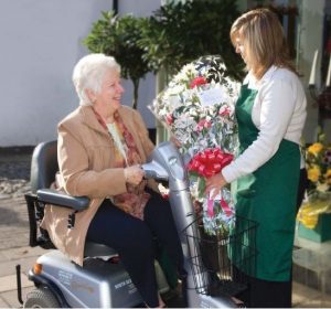 A lady on a Shopmobility scooter picking up a bouquet of flowers from a florist